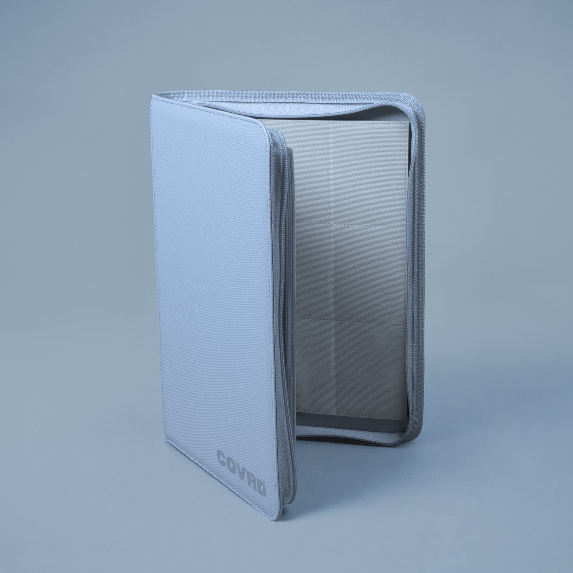 Slightly open steel blue COVRD 9-pocket card binder standing upright on a matching blue background.