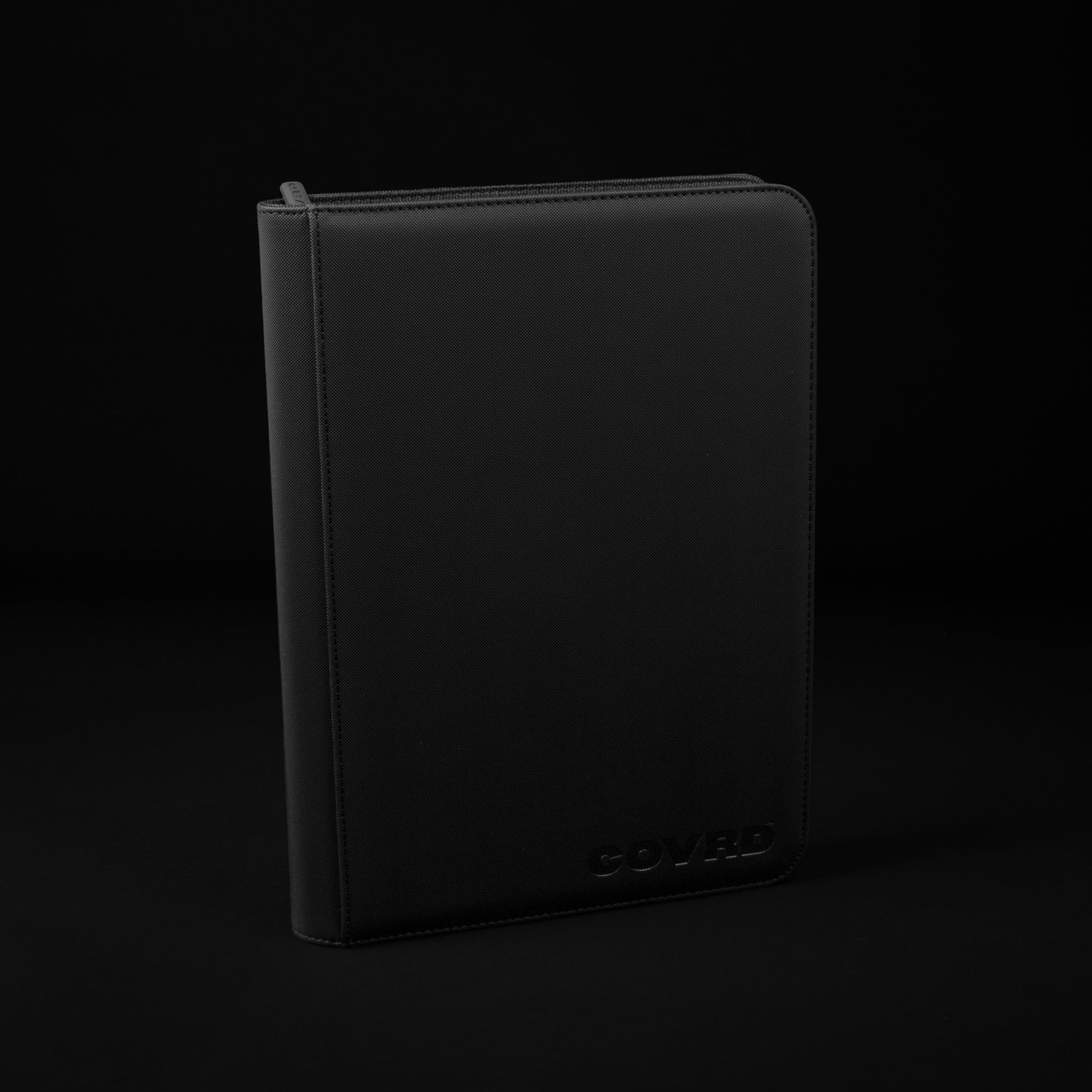 Front and spine view of black COVRD card binder standing upright showing the embossed logo.