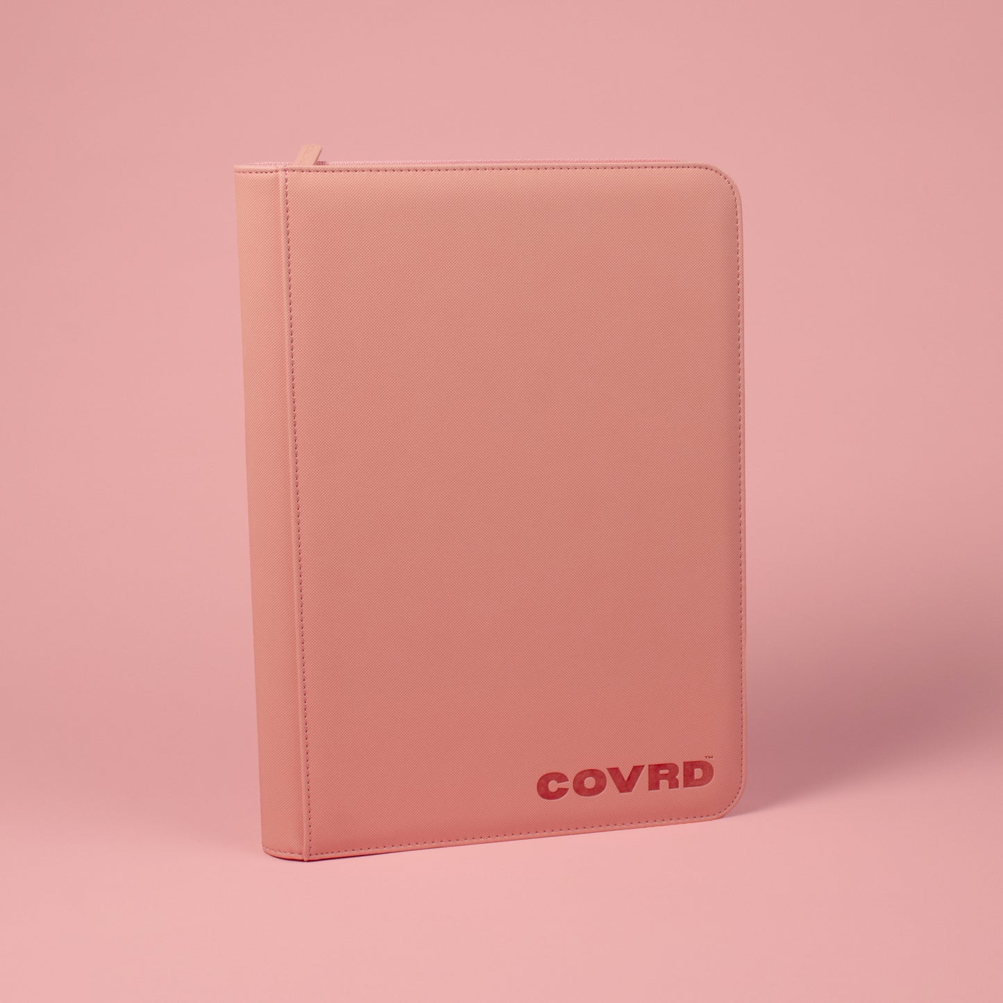 Front and spine view of blush pink COVRD card binder standing upright showing the embossed logo.