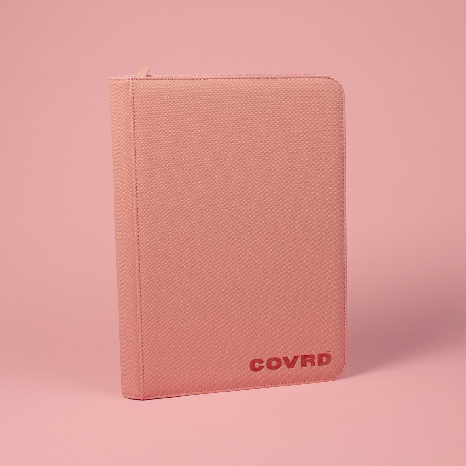 Front and spine view of blush pink COVRD card binder standing upright showing the embossed logo.