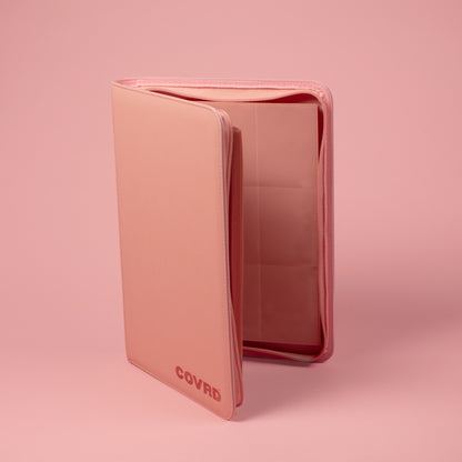 Slightly open blush pink COVRD 9-pocket card binder standing upright on a matching pink background.